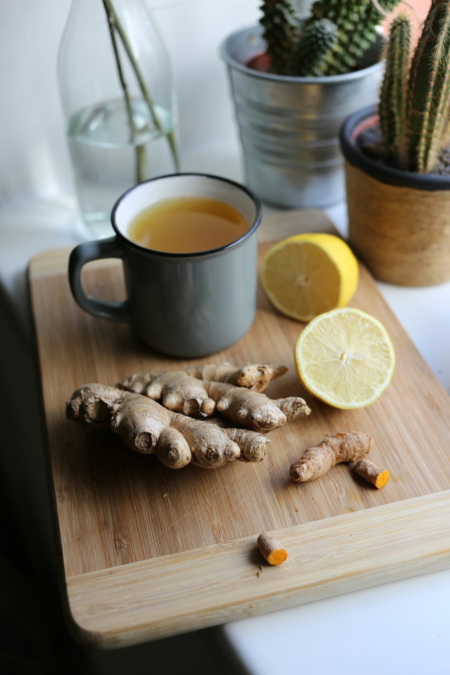 A mug of ginger shot with fresh ginger, lemon and turmeric on a board
